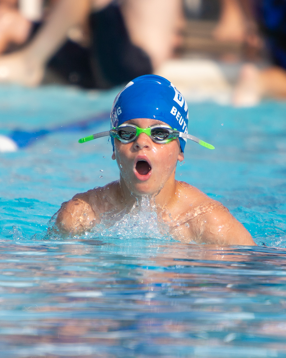 competitive youth swimmer performing breaststroke while head is appearing out of water taking a breath